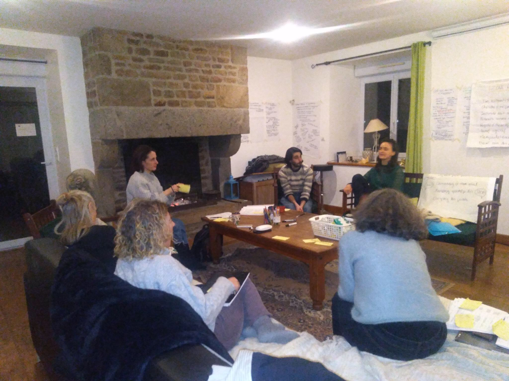 Groupe en discussion lors d'un atelier collaboratif en intérieur, dans une ambiance chaleureuse avec une cheminée et des outils de facilitation.