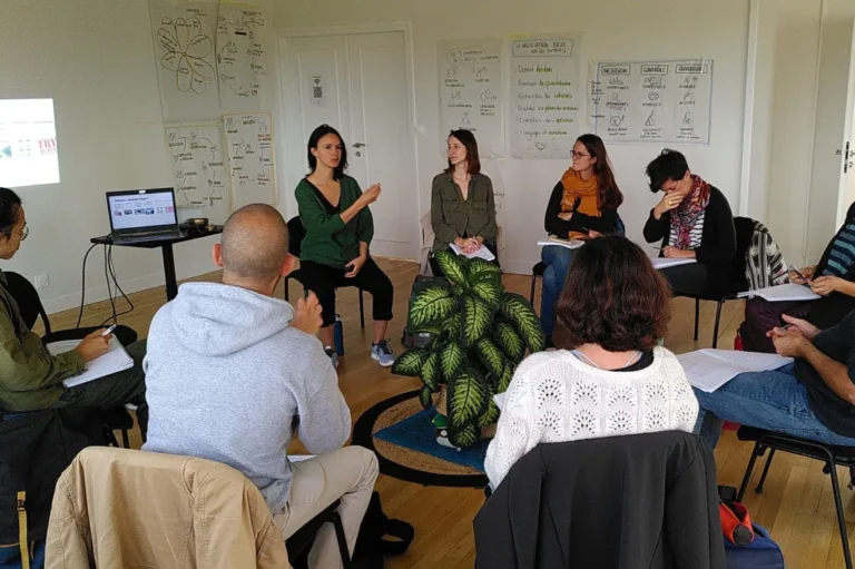 Participants en cercle lors d'un atelier de facilitation en intérieur, échangeant sur des concepts affichés au mur.